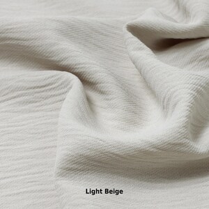 May include: Close-up of a light beige fabric with a textured surface. The fabric is soft and wrinkled, creating a natural and organic look.