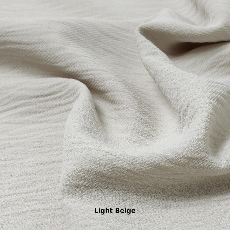 May include: Close-up of a light beige fabric with a textured surface. The fabric is soft and wrinkled, creating a natural and organic look.