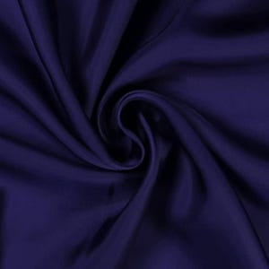 May include: A close-up shot of a deep navy blue fabric with soft folds and a silky sheen. The fabric is arranged in a swirling pattern, creating shadows and highlights that emphasize its texture and drape. The overall effect is one of luxury and elegance.