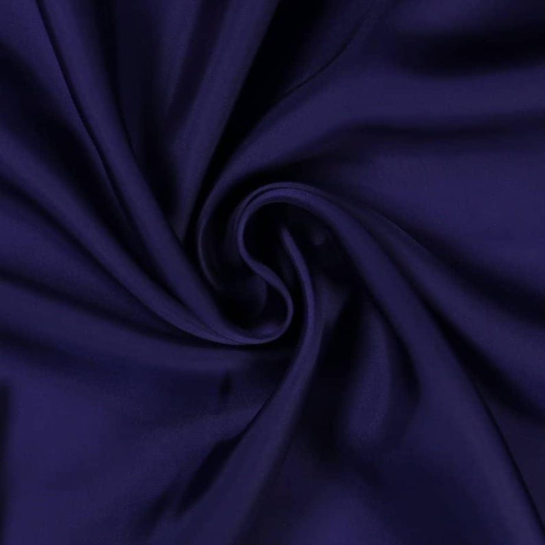 May include: A close-up shot of a deep navy blue fabric with soft folds and a silky sheen. The fabric is arranged in a swirling pattern, creating shadows and highlights that emphasize its texture and drape. The overall effect is one of luxury and elegance.