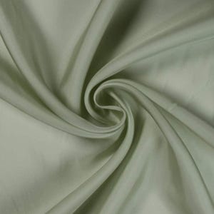 May include: Close-up of a flowing, sage green fabric with a silky sheen. The fabric is draped and swirled, creating soft folds and shadows. The material appears smooth and luxurious, suitable for apparel or home decor.
