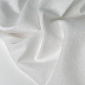 Puede incluir: Primer plano de tela blanca con pliegues suaves y superficie texturizada. La tela parece ligera y fluida, con sutiles variaciones tonales. La imagen resalta la textura y la ca&iacute;da del material.