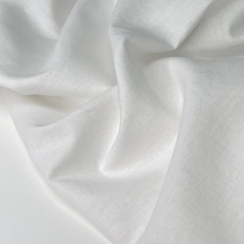 Puede incluir: Primer plano de tela blanca con pliegues suaves y superficie texturizada. La tela parece ligera y fluida, con sutiles variaciones tonales. La imagen resalta la textura y la ca&iacute;da del material.