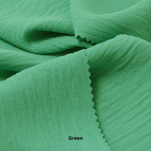 May include: Close-up of a green fabric with a textured surface. The fabric is folded in half, with the fold at the bottom of the image. The word "Green" is printed in white at the bottom of the image.