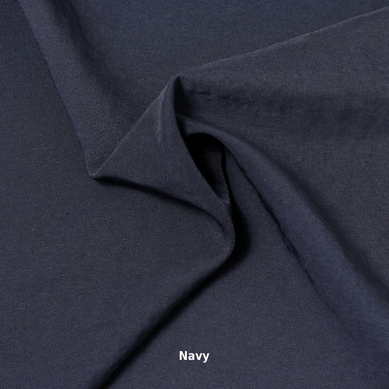 May include: A close-up of navy blue fabric with soft folds and a textured surface. The word "Navy" is printed in white at the bottom of the image. The fabric appears to be a medium weight material.