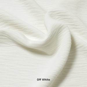 May include: Close-up of a soft, off-white fabric with a textured, crinkled surface. The fabric is smooth and has a subtle sheen.