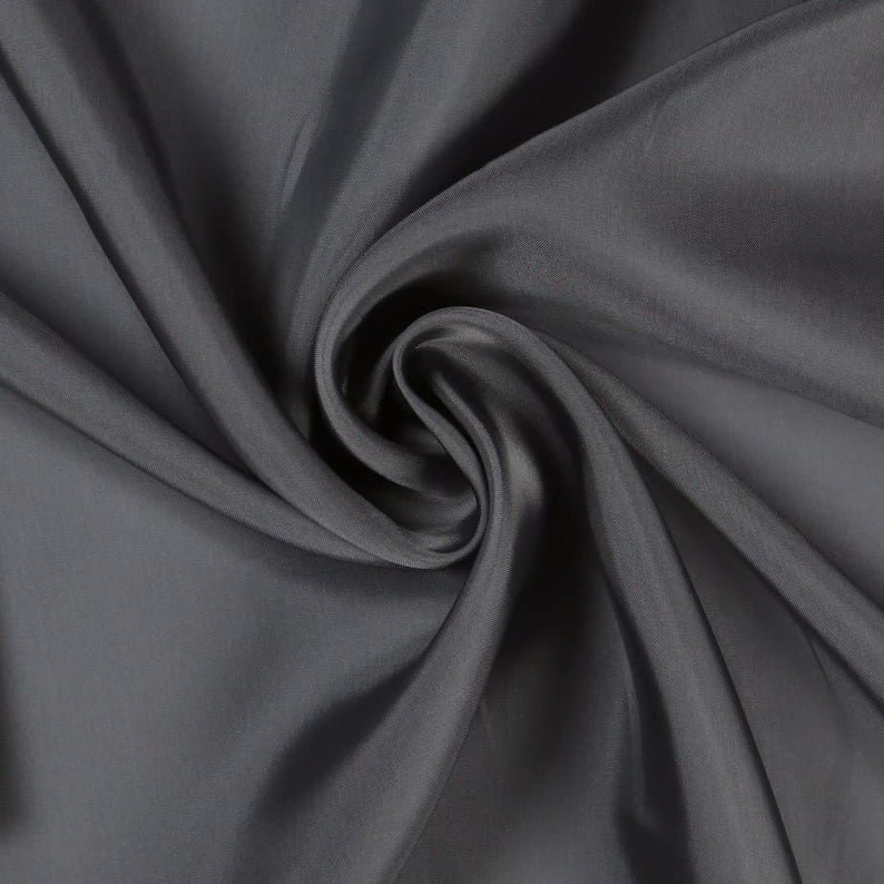 May include: Close-up of a swatch of dark gray fabric with a silky sheen. The material is draped and swirled, creating soft folds and shadows. The fabric appears smooth and luxurious, suitable for apparel or home decor.