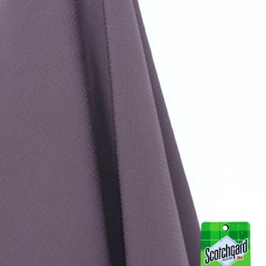 Pode incluir: Uma amostra de tecido roxo com uma superfície texturizada. A palavra "Purple" está impressa na parte inferior. Uma etiqueta verde e branca Scotchgard Water Repellent está anexada, indicando que o tecido repele a chuva e outros líquidos.