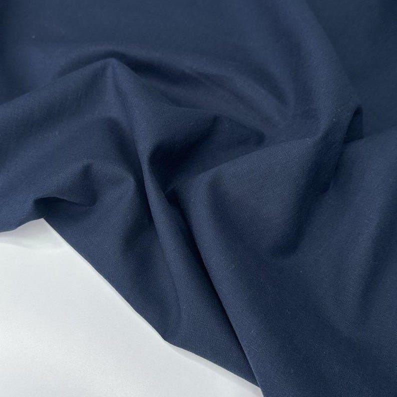 Puede incluir: Primer plano de tela azul marino con pliegues suaves y textura lisa. La tela es de color azul oscuro s&oacute;lido, y los pliegues crean sombras y reflejos, agregando profundidad a la imagen. La tela parece ser un material de peso medio.