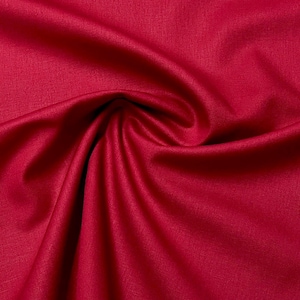 May include: Close-up of a deep red fabric with a smooth, slightly textured surface. The fabric is folded and draped, showcasing its soft and flowing nature.