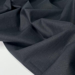 Puede incluir: Primer plano de una tela negra oscura con textura y pliegues visibles. El material parece ser un textil tejido, posiblemente lino o una fibra natural similar. La tela es de color uniforme y tiene un acabado mate.