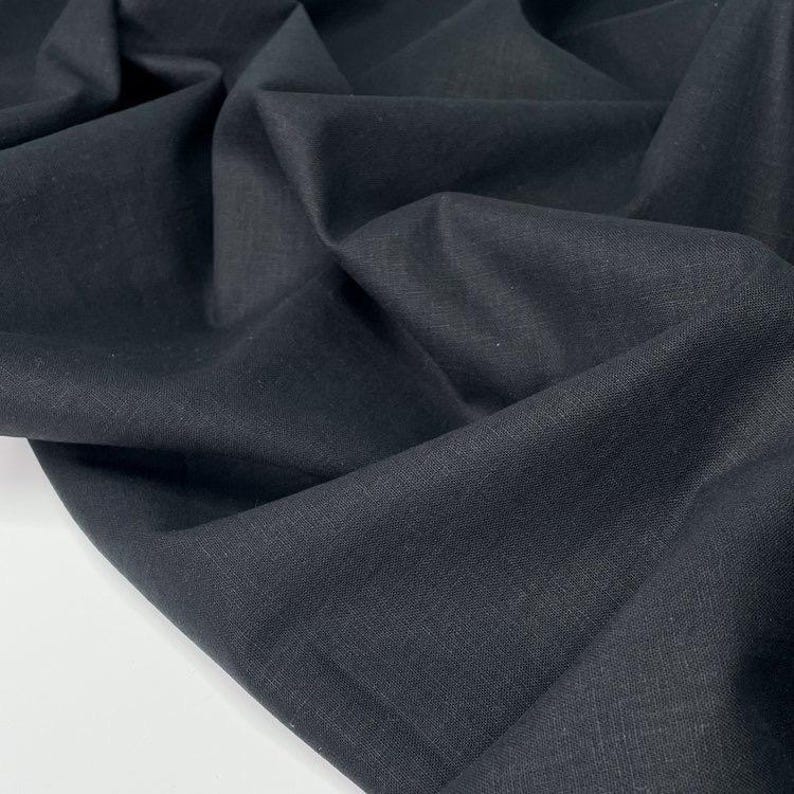 Puede incluir: Primer plano de una tela negra oscura con textura y pliegues visibles. El material parece ser un textil tejido, posiblemente lino o una fibra natural similar. La tela es de color uniforme y tiene un acabado mate.