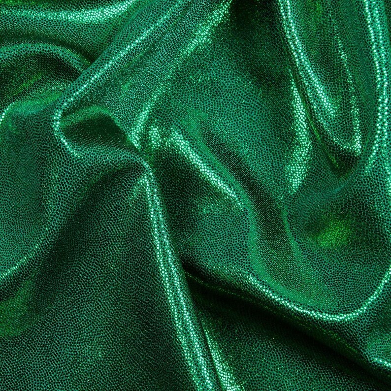 May include: Green iridescent fabric with a textured, sparkly finish. The fabric is wrinkled and folded.