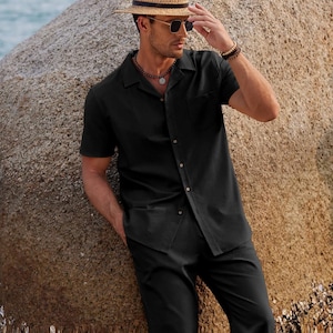 Puede incluir: Camisa negra de manga corta y pantalón a juego. La camisa tiene un bolsillo en el pecho. La persona lleva un sombrero de paja, gafas de sol y un collar. El atuendo es adecuado para el clima cálido.