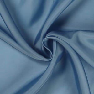 May include: Close-up of a flowing, light blue fabric with a silky sheen. The fabric is draped and folded, creating soft shadows and highlights. The material appears smooth and luxurious, suitable for apparel or home decor.