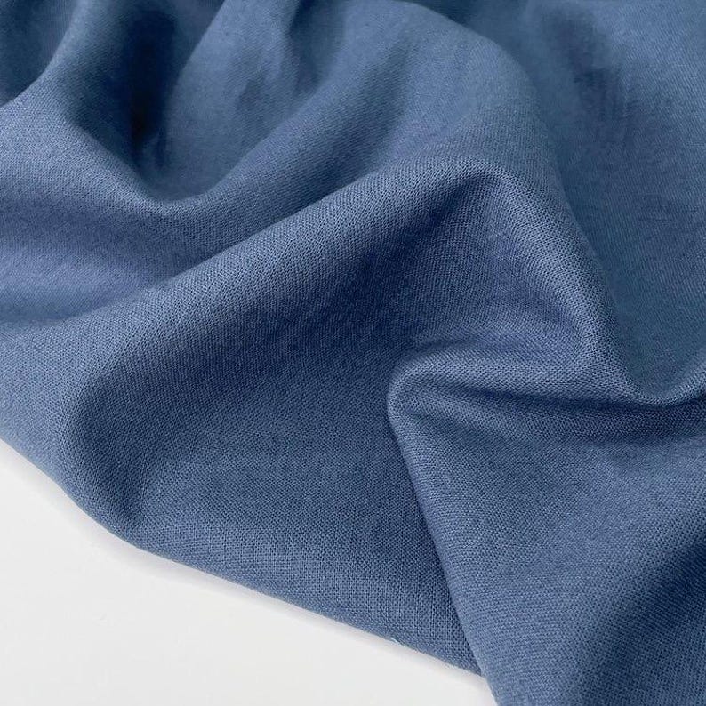 Puede incluir: Primer plano de una tela azul texturizada con pliegues suaves. La tela tiene un acabado mate y una textura ligeramente irregular, lo que sugiere una fibra natural como el lino o el algod&oacute;n. El color es un azul apagado.