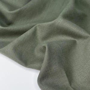 Puede incluir: Primer plano de tela verde oliva con textura y pliegues visibles. La tela parece ser una fibra natural, posiblemente lino o algod&oacute;n, con un acabado ligeramente mate. El color es un tono apagado y terroso.