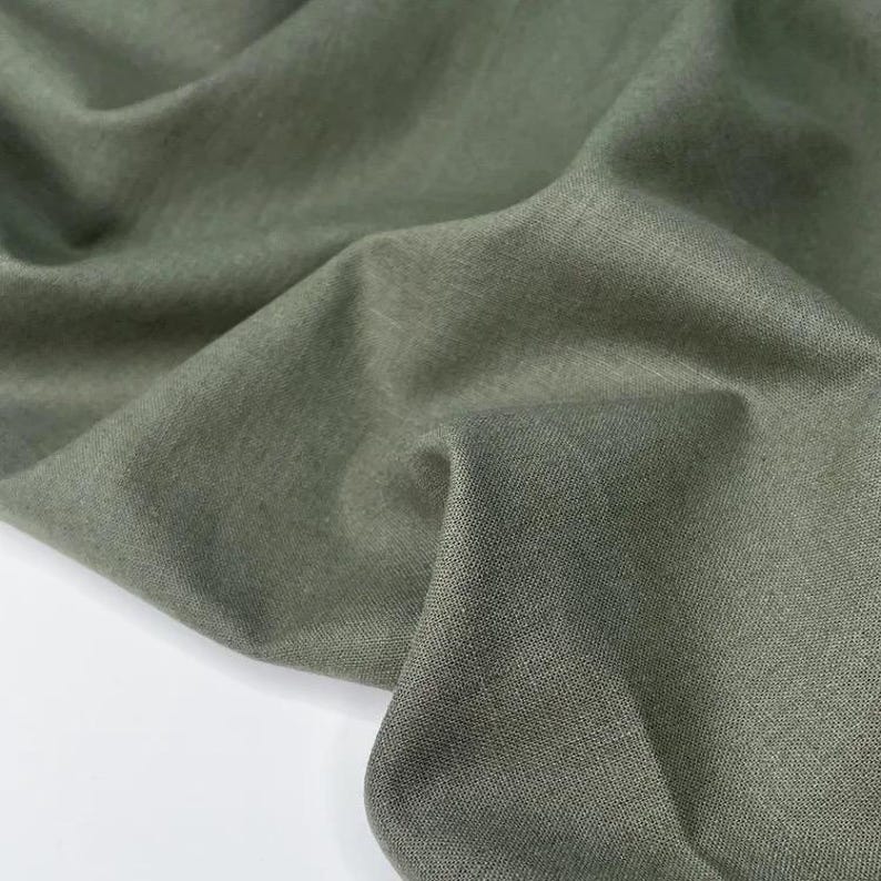 Puede incluir: Primer plano de tela verde oliva con textura y pliegues visibles. La tela parece ser una fibra natural, posiblemente lino o algod&oacute;n, con un acabado ligeramente mate. El color es un tono apagado y terroso.