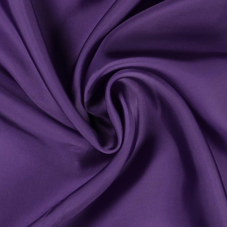 May include: Close-up of a deep purple fabric with a silky texture. The fabric is draped and folded, creating soft shadows and highlights. The color is a rich, saturated shade of purple.