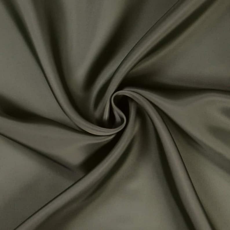 May include: Close-up of olive green fabric with soft folds and a swirling pattern. The fabric has a subtle sheen, creating highlights and shadows. The material appears smooth and luxurious, suitable for apparel or home decor.