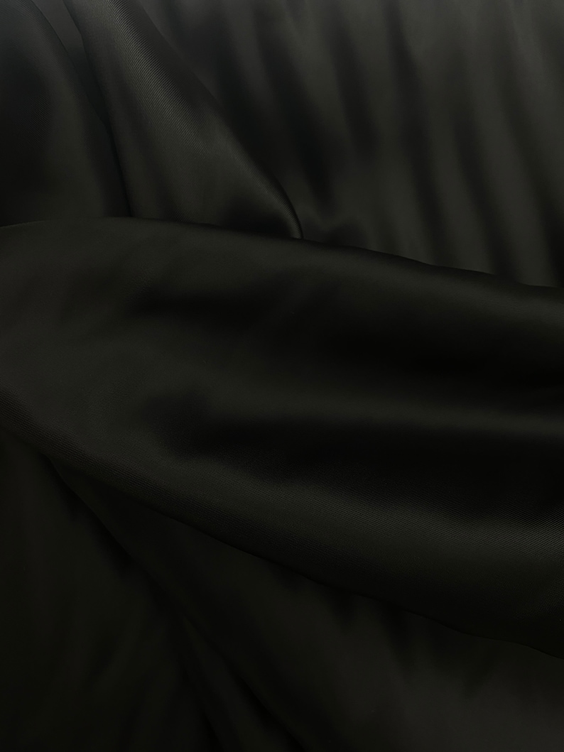 Puede incluir: Tela negra con una textura suave y sedosa. La tela est&aacute; drapeada y doblada, creando l&iacute;neas suaves y fluidas.