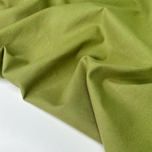 Puede incluir: Primer plano de una tela verde oliva doblada. La tela tiene un aspecto ligeramente texturizado y est&aacute; drapeada en pliegues suaves. El color es un verde apagado y terroso, con sutiles variaciones de tono debido a los pliegues y la iluminaci&oacute;n. La tela parece ser de peso medio.