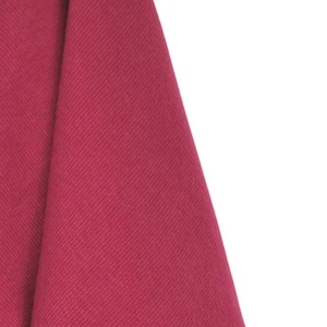 Puede incluir: Primer plano de una tela doblada y texturizada en color magenta intenso. La tela tiene un patrón acanalado y es parcialmente visible sobre un fondo blanco. El material parece suave y flexible.
