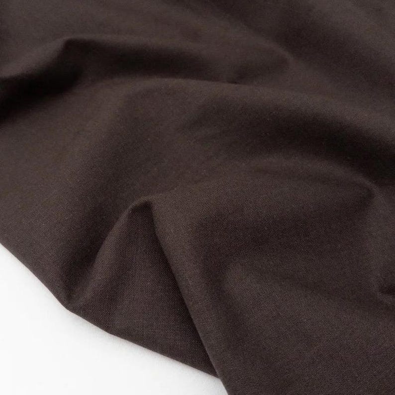 Puede incluir: Primer plano de una tela marr&oacute;n oscuro con textura y pliegues visibles. El material parece ser un textil tejido, posiblemente lino o algod&oacute;n, con un acabado mate. El color es un tono profundo y terroso.