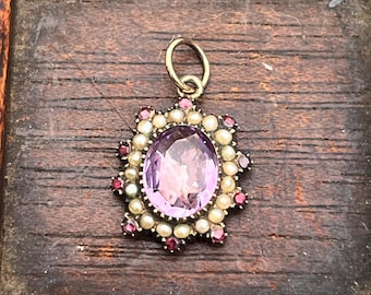 May include: A gold pendant with a large oval amethyst gemstone surrounded by a halo of small pearls and red gemstones.