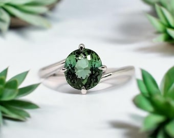 May include: A silver ring with a green gemstone set in a four-prong setting. The ring has a twisted band.
