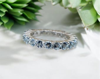 May include: A silver eternity band ring with a row of light blue aquamarine gemstones.