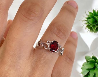 Puede incluir: Un anillo de plata con una piedra ovalada roja engastada en un diseño delicado y ornamentado.