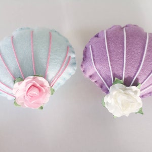 May include: Two felt seashells with pink and white fabric flowers. The seashells are light blue and purple.