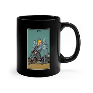 May include: Black ceramic mug with a white image of the Seven of Swords tarot card. The card depicts a figure in a blue tunic and red hat carrying seven swords away from a castle.