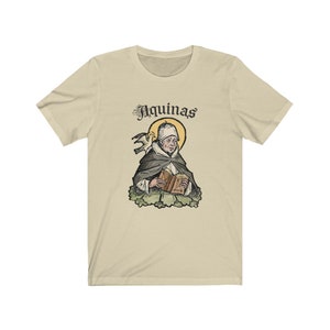 May include: A beige t-shirt with a vintage illustration of a man holding a book. The illustration is surrounded by a yellow halo and the text "Aquinas" is above the image.
