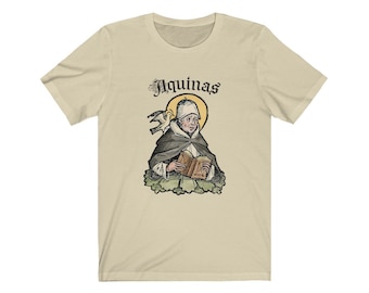 Pode incluir: Uma camiseta bege com uma ilustração vintage de um homem segurando um livro. A ilustração é cercada por um halo amarelo e o texto "Aquinas" está acima da imagem.