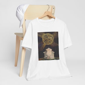 May include: White t-shirt with a print of a painting depicting a person kneeling with their head bowed under a large, golden sun.