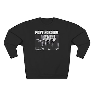 Pode incluir: Camisola preta com a inscrição "POST FORDISM". O gráfico a preto e branco mostra duas figuras com cabeças de monitor de computador. Camisola de gola redonda.