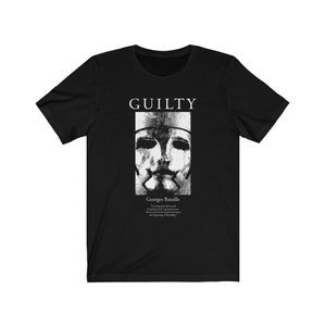 May include: Black t-shirt with a white graphic design featuring a face with a mask and the text "GUILTY" and "Georges Bataille".