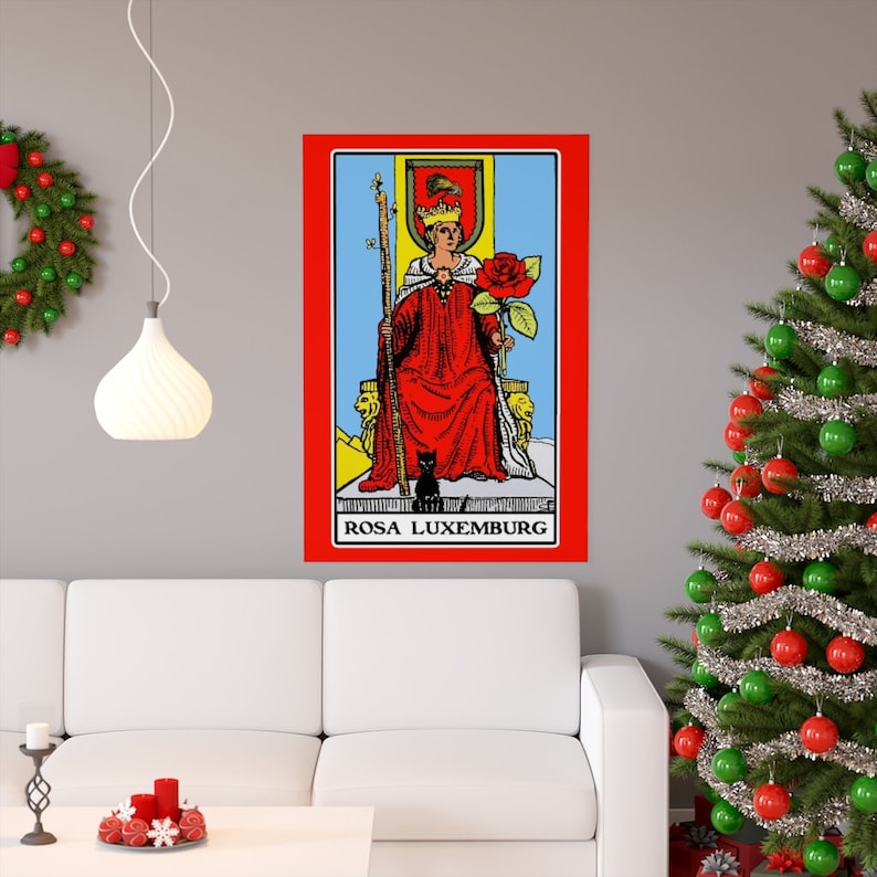 May include: A tarot card illustration of the Queen of Wands. The Queen is sitting on a throne with a red robe, a crown, and a staff. She is holding a red rose in her right hand. A black cat is sitting at her feet. The card is titled "ROSA LUXEMBURG".
