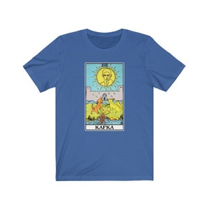 Puede incluir: Una camiseta azul con un gráfico de una carta de tarot que presenta la cara de un hombre en el sol, tres perros y la palabra "Kafka".