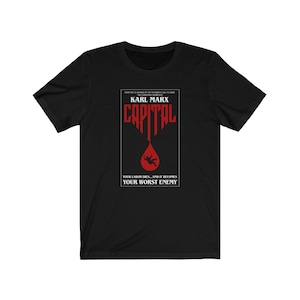 Może przedstawiać: Czarny T-shirt z czerwoną grafiką przedstawiającą okładkę książki zatytułowaną "Kapitał" autorstwa Karola Marksa. Grafika przedstawia czerwoną kroplę krwi, w którą spada sylwetka osoby. Tekst pod grafiką brzmi: "Twoja praca umiera... i staje się twoim najgorszym wrogiem."
