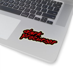 May include: A laptop computer with a sticker that says "dark precursor" in red and yellow lettering on a white background.