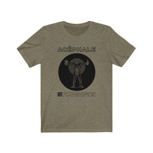 May include: Olive green t-shirt with the word "ACÉPHALE" in black, above a black circle containing a human figure illustration. Below the circle is text in a smaller font. The shirt is made of a soft material.