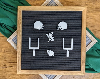 May include: A black letter board with white football-themed decorations. The decorations include two football helmets, two goal posts, a football, and the word "VS" with a lightning bolt.
