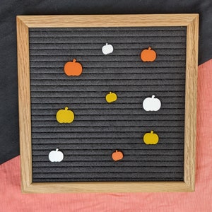 May include: A black letter board with a wooden frame, decorated with orange and yellow pumpkin shapes and white pumpkin shapes.