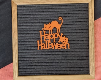 Może przedstawiać: Czarna tablica z literami z drewnianą ramą. Tablica ma pomarańczowe filcowe litery, które piszą "Happy Halloween" z wycięciem czarnego kota i dyni.