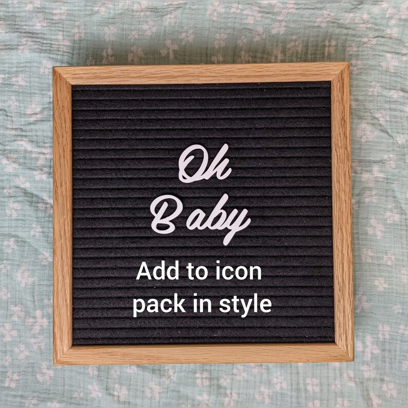 Peut inclure: Un tableau d'affichage noir avec un cadre en bois blanc. Le tableau affiche "Oh Baby" en &eacute;criture cursive et "Add to icon pack in style" en police sans serif.