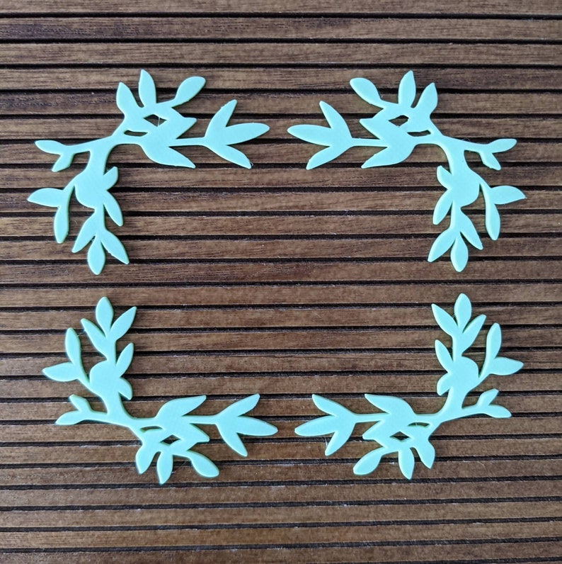 May include: Four light blue paper cutouts of leafy branches arranged in a square frame on a brown wooden background.