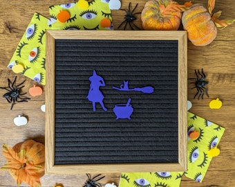 May include: A black letter board with a purple witch, cat, cauldron, and broom silhouette. The board is surrounded by Halloween decorations, including pumpkins, spiders, and eyes.